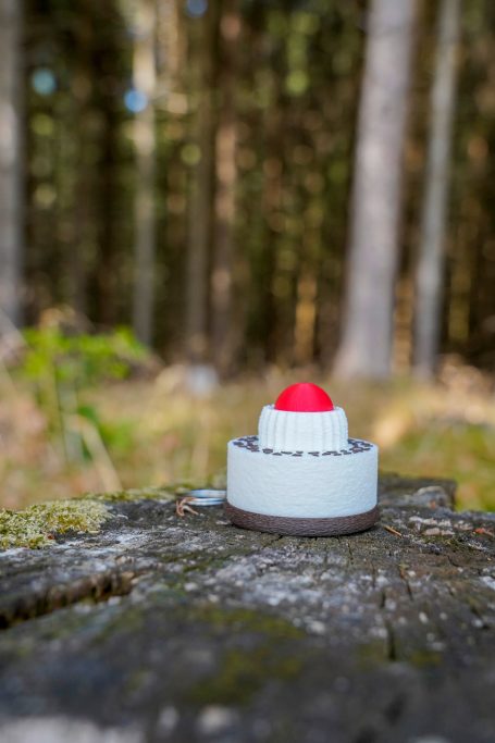 Schwarzwälder Kirschtorten-Klicker auf einem Holzstamm vor einem Waldhintergrund